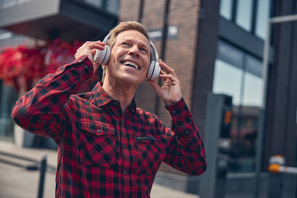 Joyful man listening to music through wireless headphones - Foto, afbeelding