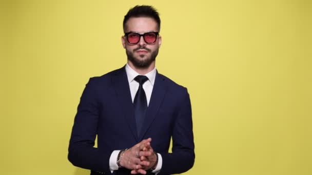 sexy unrasierte Geschäftsmann im Anzug mit Sonnenbrille berühren die Hände und reiben die Handflächen, Blick zur Seite und nach unten auf gelbem Hintergrund - Filmmaterial, Video