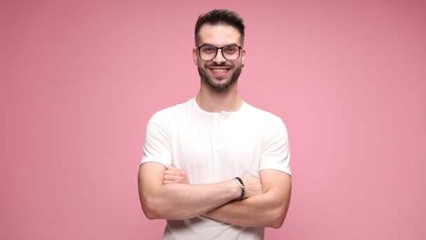 σέξι casual τύπος στέκεται με σταυρωμένα τα χέρια του, φοράει γυαλιά, χαμογελά πλατιά, δίνει ένα αντίχειρες με τα δύο χέρια σε ροζ φόντο - Πλάνα, βίντεο