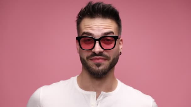 close up of a casual guy being happily surprised, amused, drunk and starting to laugh and point his finger forward, sticking his tongue out and fooling around against pink background - Footage, Video