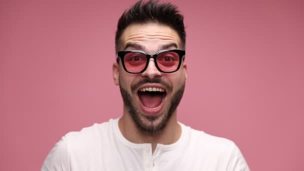 close up of an attractive casual man having a fearfully surprised, surprised, happily surprised expression on his face, yelling out loud, running hands trough hair, and couldn't believe what is happening on pink background - Footage, Video