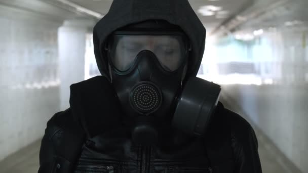 Mann mit Gasmaske, schwarzer Jacke mit Kapuze geht durch langen Tunnel, Unterführung - Filmmaterial, Video
