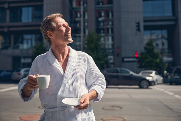 Handsome joyful man in bathrobe standing on the street - Foto, Bild