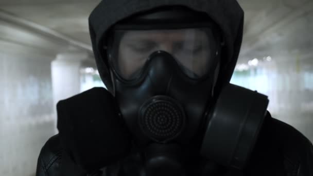 mężczyzna w masce gazowej, czarna kurtka z kapturem przechodzącym przez długi tunel, przejście podziemne - Materiał filmowy, wideo