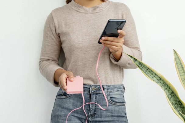 Ruka mladé ženy držící chytrý telefon a moderní nabíječku náhradních baterií Stůjte a nabíjejte smartphone s nabíječkou záložní baterie v ruce. - Fotografie, Obrázek