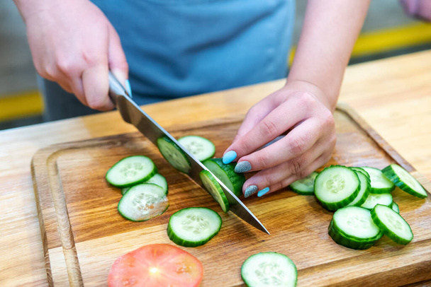 female hands cut cucumber into slices on a wooden cutting board - Photo, image