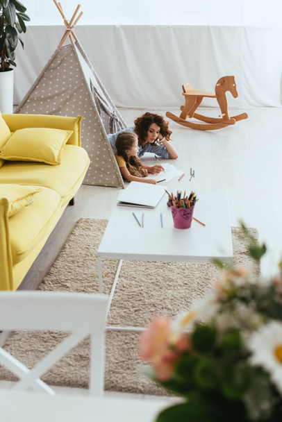 high angle view of babysitter and child drawing while lying in toy wigwam - Foto, immagini