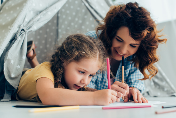 happy babysitter and adorable child drawing together in play tent - Photo, Image