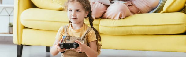 KYIV, UKRAINE - JUNE 19, 2020: cropped view of nanny on sofa and kid playing video game with joystick, horizontal image - Foto, imagen