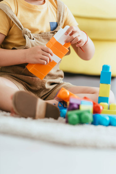 partial view of child sitting on floor and playing with multicolored building blocks, selective focus - Foto, Imagen