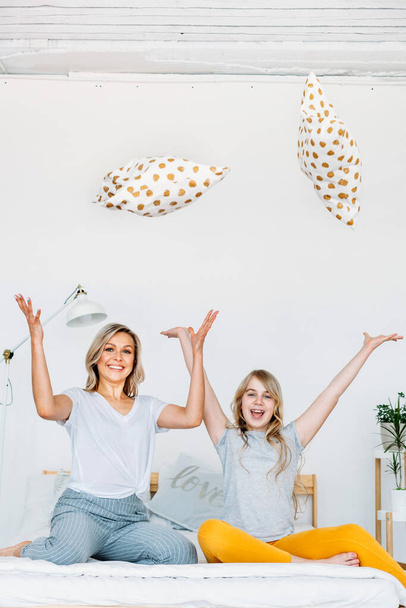 Mother and daughter sit on the bed and throw pillows to the top, joy and fun, communication, family, style, morning - 写真・画像