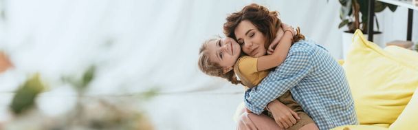 horizontal image of happy nanny hugging smiling kid while sitting on sofa - Photo, Image