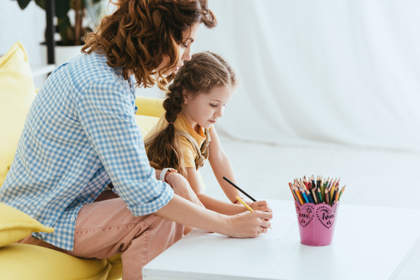 young babysitter and cute kid drawing with pencils together - Photo, Image