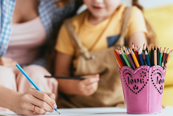 enfoque selectivo del dibujo de la niñera con lápiz cerca del niño y porta bolígrafos en la mesa - Foto, Imagen