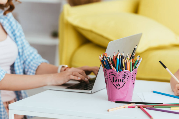 Kalem tutacağının yanındaki masadaki dizüstü bilgisayarda renkli kalemler ve aşk yazılarıyla serbest çalışanın kırpılmış görüntüsü - Fotoğraf, Görsel