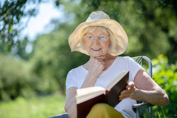Excited elderly woman reading an interesting book - Zdjęcie, obraz