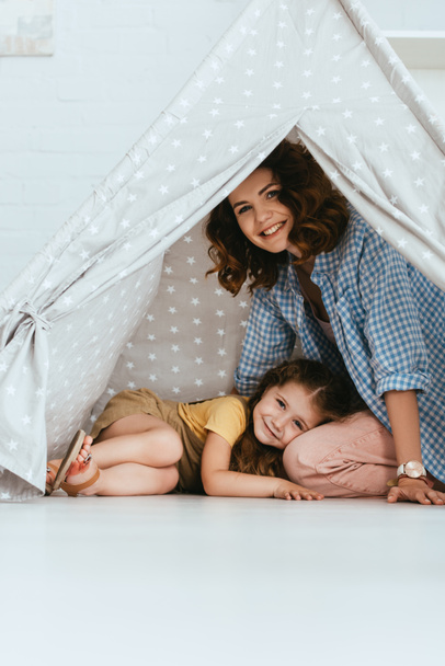 happy kid lying on laps of smiling nanny in play tent at home - Photo, Image