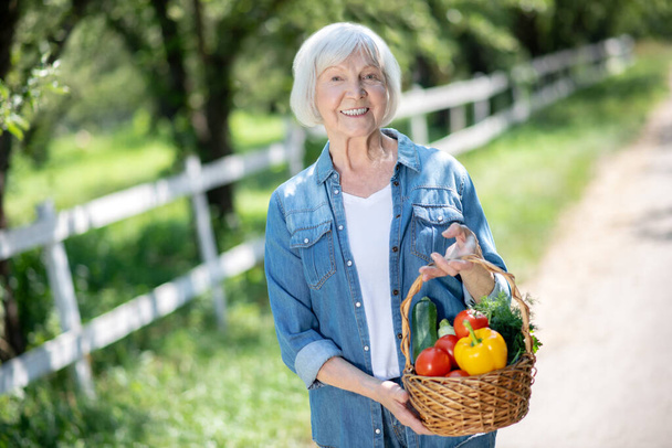Smiling woman holding a basket of fresh seasonal vegetable - Zdjęcie, obraz