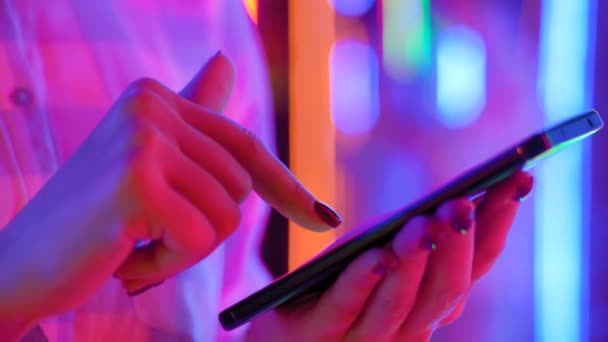 Κλείσιμο προβολής: γυναίκα χέρια χρησιμοποιώντας smartphone κατά το φως πολύχρωμο φόντο - Πλάνα, βίντεο