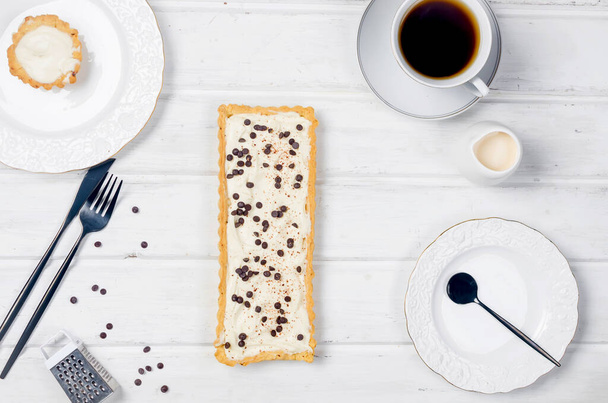 tart with vanilla cream or cheesecake with chocolate drops and cup of coffee on white wooden table, copy space, top view - Photo, image