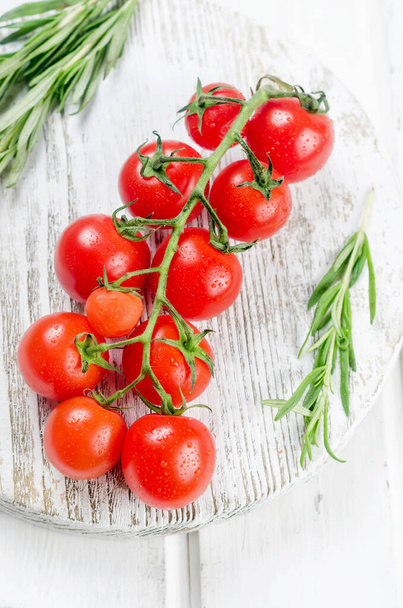 Bunch of juicy organic red cherry tomatoes with green  rosemary,  garlic and spices on white old table. Ingredients for cooking. Clean eating concept. Vegetarian diet. space for text - Zdjęcie, obraz