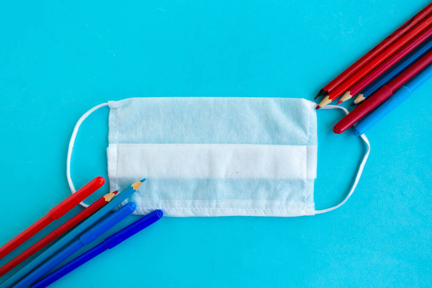 Színes ceruzák és orvosi maszk kék alapon, felülnézetből. Vissza az iskolába koncepció, iskolai karantén koncepció - Fotó, kép