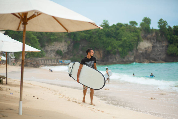 Surfer. Surfing Man With Surfboard Walking On Sandy tropical Beach. Healthy Lifestyle, water activities, Water Sport. Beautiful Ocean. Bali, Indonesia - 03/24/2018 - Fotó, kép