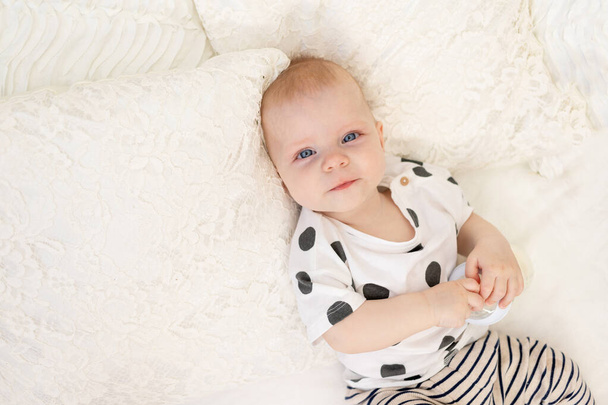 bébé de 8 mois couché sur le lit à la maison en pyjama avec un biberon de lait, concept de nourriture pour bébé, lait de succion pour bébé, endroit pour le texte - Photo, image