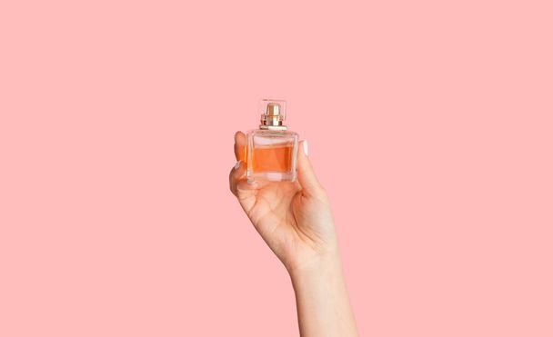 Primer plano de la mano femenina mostrando botella de vidrio con perfume sobre fondo rosa
 - Foto, imagen