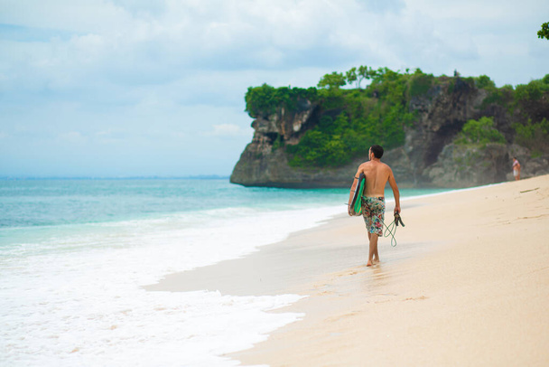 Surfista. Surfing Man With Surfboard Walking On Sandy tropical Beach (en inglés). Estilo de vida saludable, actividades acuáticas, Deportes acuáticos. Hermoso océano - Foto, Imagen
