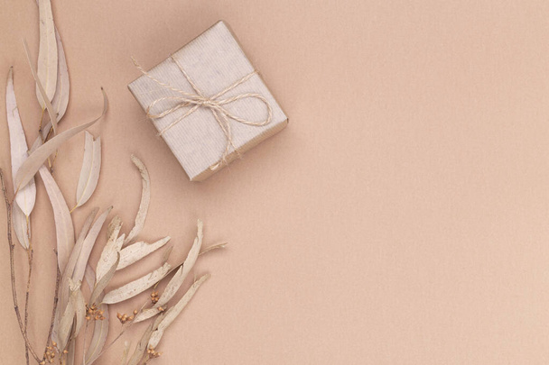 Autumn composition. Gifts wrapped in kraft paper, autumn eucalyptus leaves, on a beige background. Flat lay, top view, copy space. - Photo, image