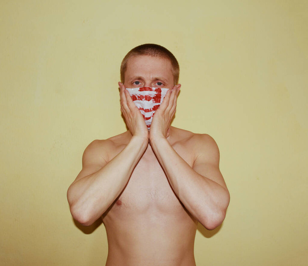 Mladý nahý muž v masce s krví drží hlavu na žlutém pozadí - Fotografie, Obrázek