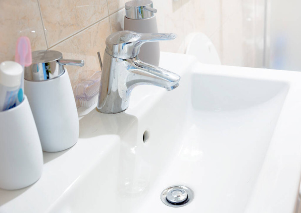 bílý keramický dřez s chromovaným kohoutkem s nádobami na mýdlo a kartáček na zuby v koupelně. Interiér domu. - Fotografie, Obrázek