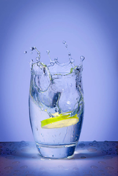 Fetta di limone cade su acqua minerale e spruzzi d'acqua  - Foto, immagini