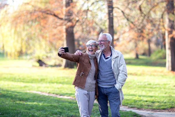 Aged man and woman taking selfie in park - Fotoğraf, Görsel