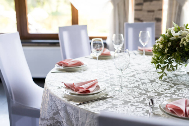Mesa festiva con copas de vino y flores frescas. Banquete de selebración con servilletas rosadas, platos blancos y anteojos de vino en restaurante
 - Foto, imagen