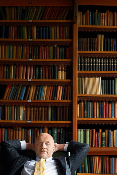 Businessman Sitting in Library hands behind head - Foto, afbeelding