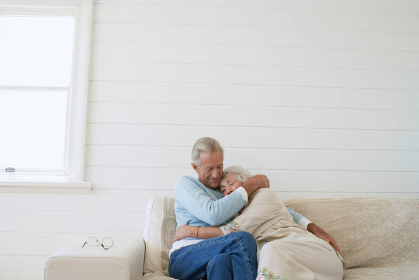 Idős pár ölelkezve ül a kanapén a nappaliban - Fotó, kép