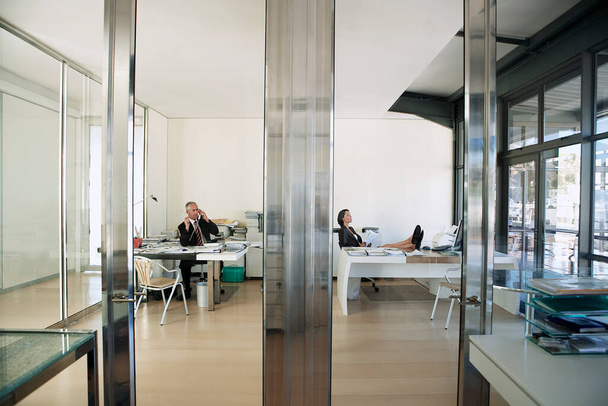 View through transparent doors of businessman working in office while businesswoman relaxes. - Photo, image