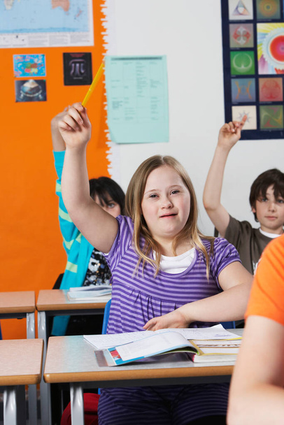 Girl (10-12) with Down syndrome raising hand in classroom - 写真・画像