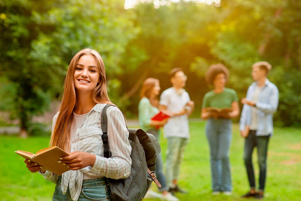 Feliz estudiante sonriente sosteniendo libro posando al aire libre en el campus universitario
 - Foto, Imagen