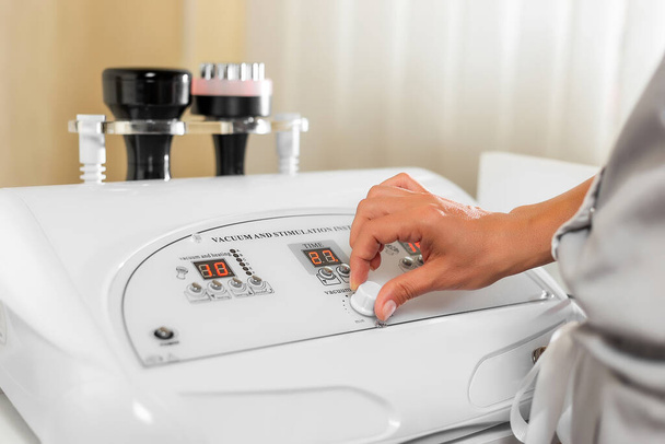 A mão da mulher especialista em massagem ajusta a máquina de vácuo para massagem anti-celulite. Máquina de lipomassagem. massagem no salão de beleza. Massagem de anticelulite
. - Foto, Imagem