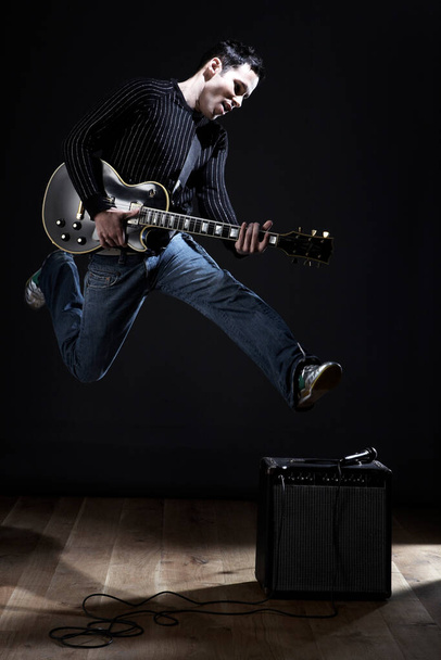 Young man with electric guitar jumping on stage - Foto, Bild
