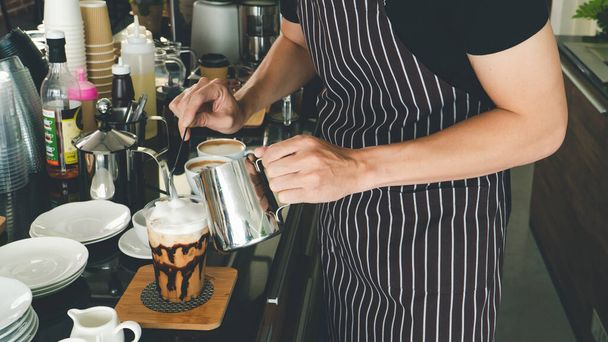 lähikuva kädestä kaataa tuoretta cappuccinoa lasiin. barista Professional miehet tekevät latte ja espresso asiakaspalveluun. kahvilan omistaja valmistaa juomia kahvilassa. - Valokuva, kuva