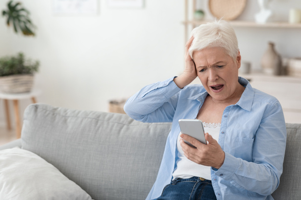 Mobile Scams Concept. Shocked Senior Woman Looking At Smartphone Screen In Frustration - Фото, изображение