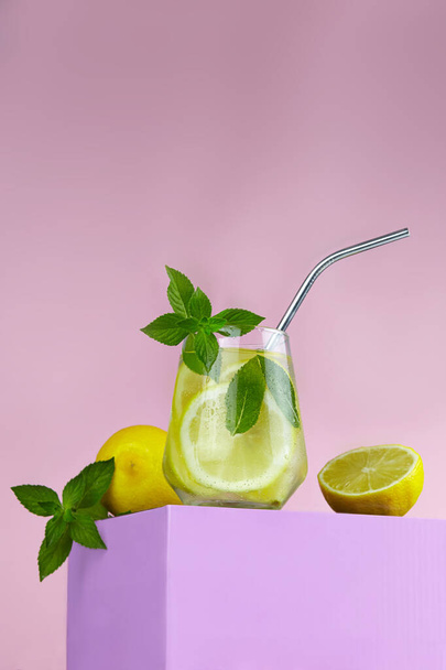 Cold lemonade with lemon in glass with ice. Refreshing summer cocktail with metal straw on a color background. - Fotó, kép
