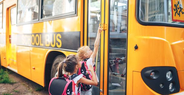 Schoolgirls with backpacks enter the school bus, back to school. - Photo, Image
