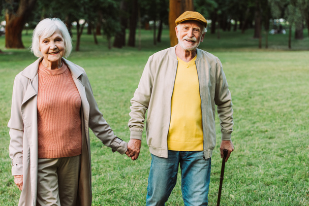 公園を歩いている間に手を取り合っている積極的な老夫婦  - 写真・画像