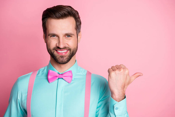 Photo of handsome guy trend clothes direct thumb finger side empty space toothy smile showing novelty banner wear shirt suspenders bow tie isolated pastel pink color background - Foto, Imagem
