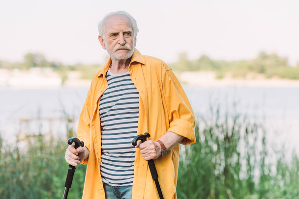 Starszy mężczyzna trzymający laseczki podczas oglądania się w parku  - Zdjęcie, obraz